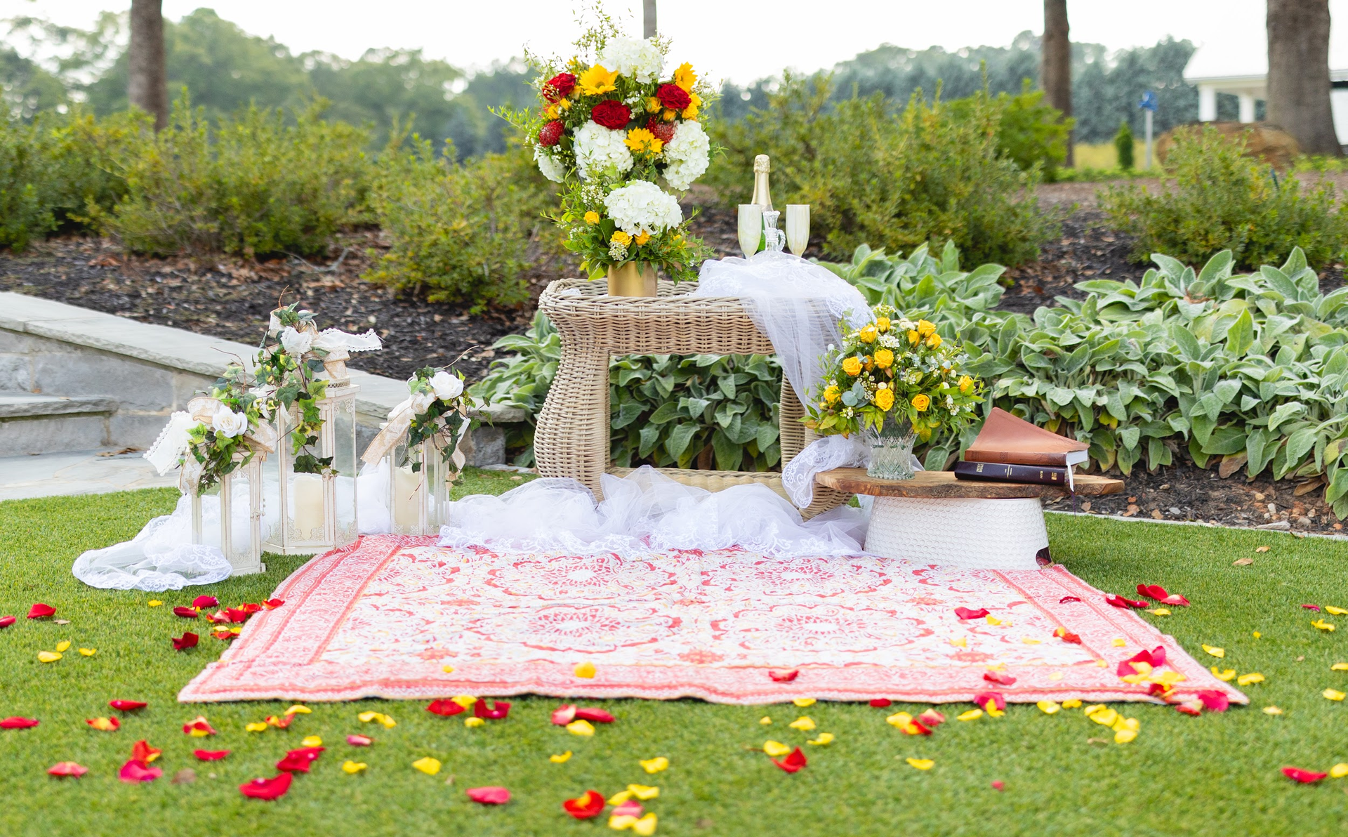 A rug is sitting on the grass next to a table with flowers on it.