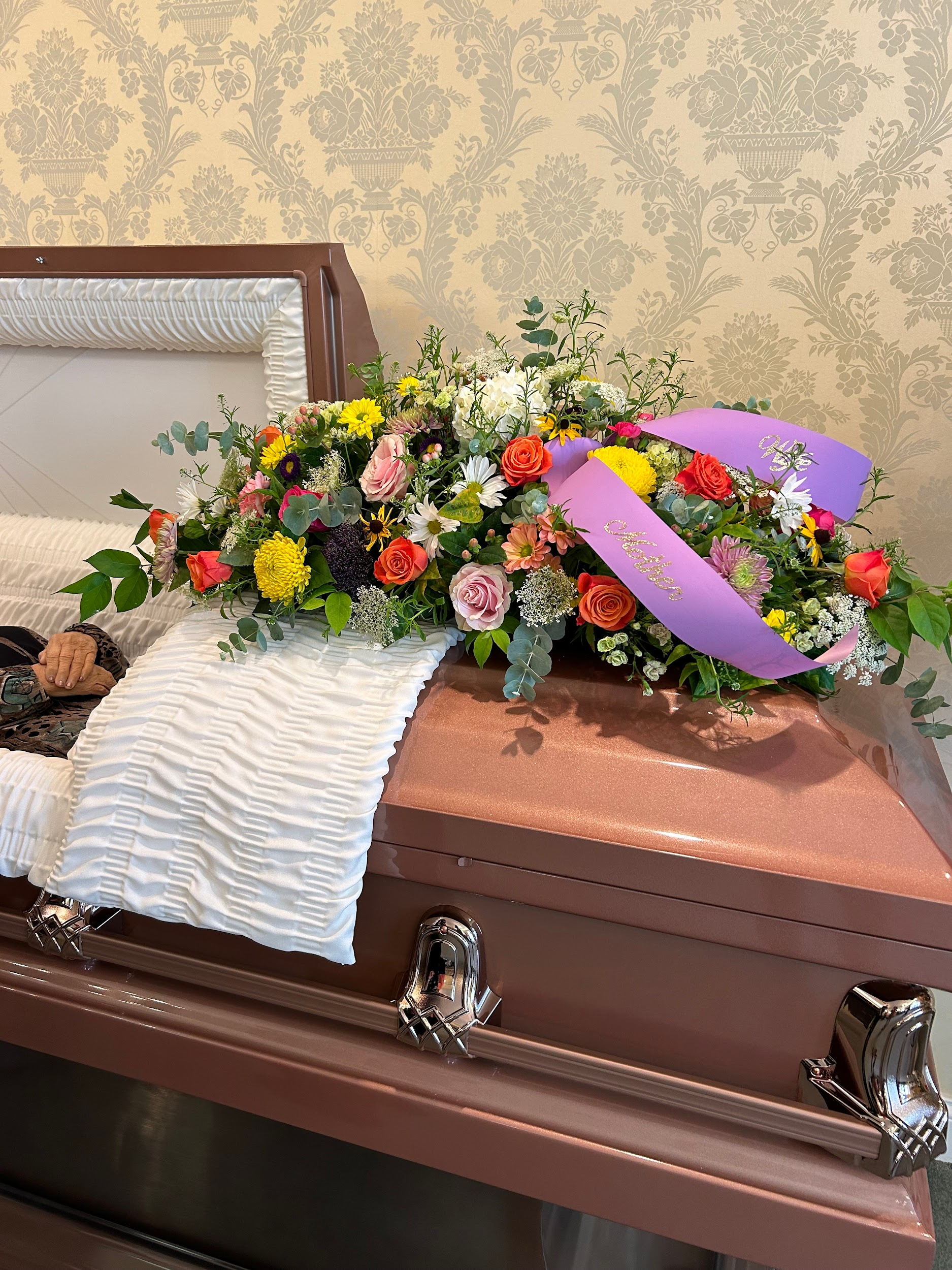 A coffin with flowers and a purple ribbon on top of it.