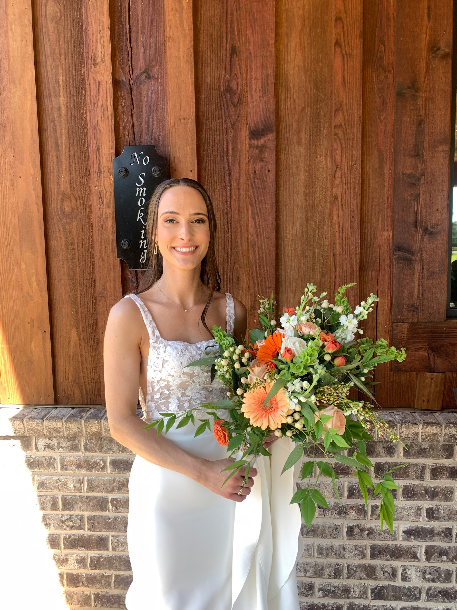 A bride in a white dress is holding a bouquet of flowers in front of a wooden wall.