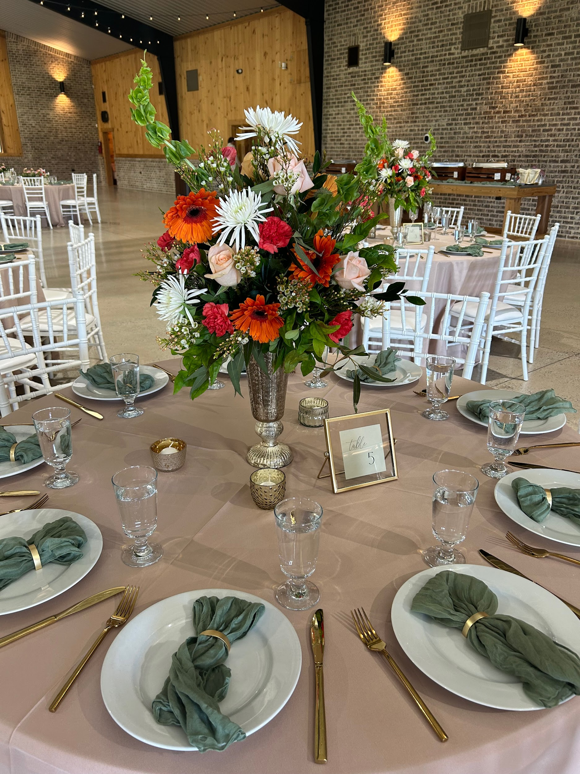 A table set for a wedding reception with plates , utensils , and a vase of flowers.