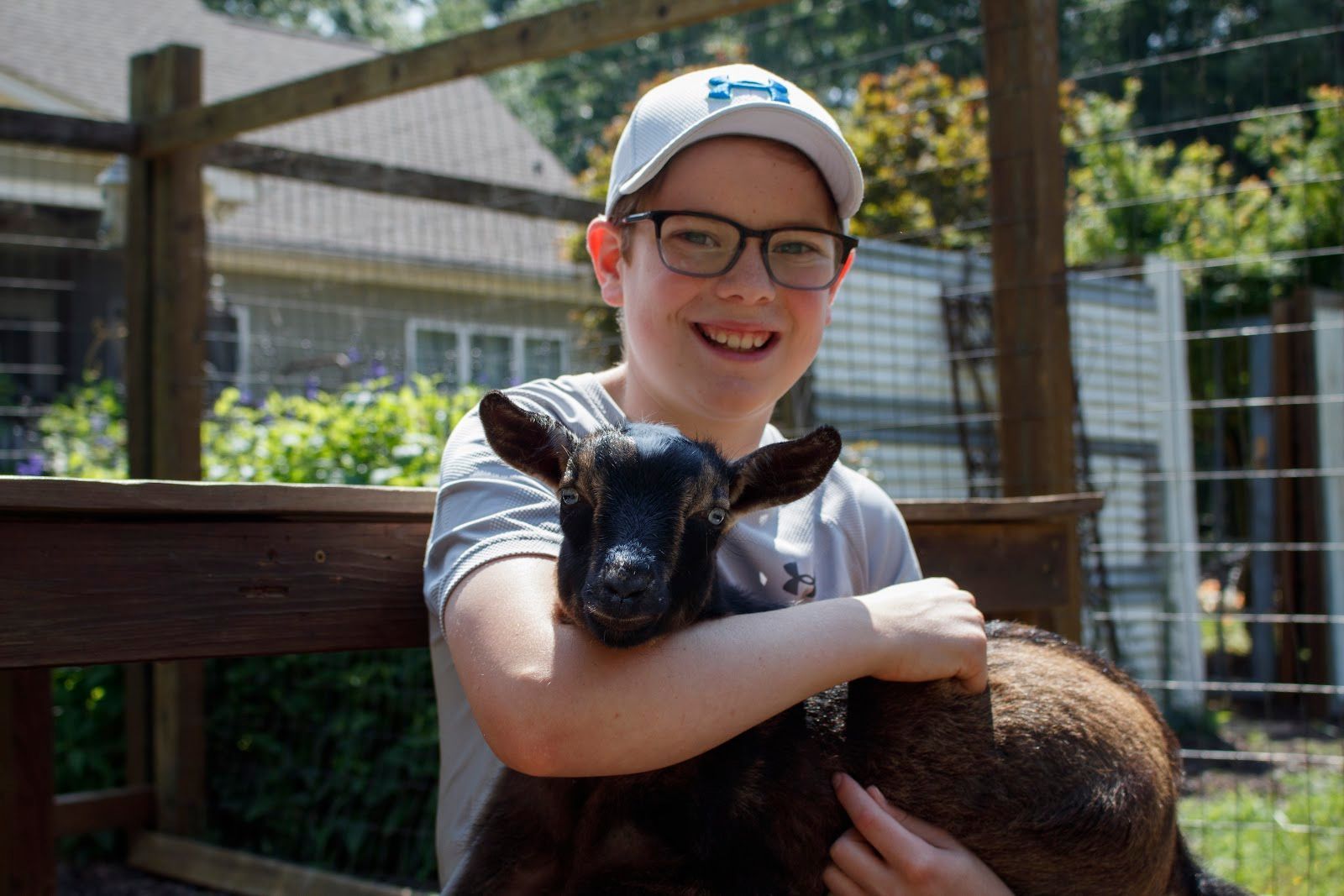 A young boy is holding a small goat in his arms.