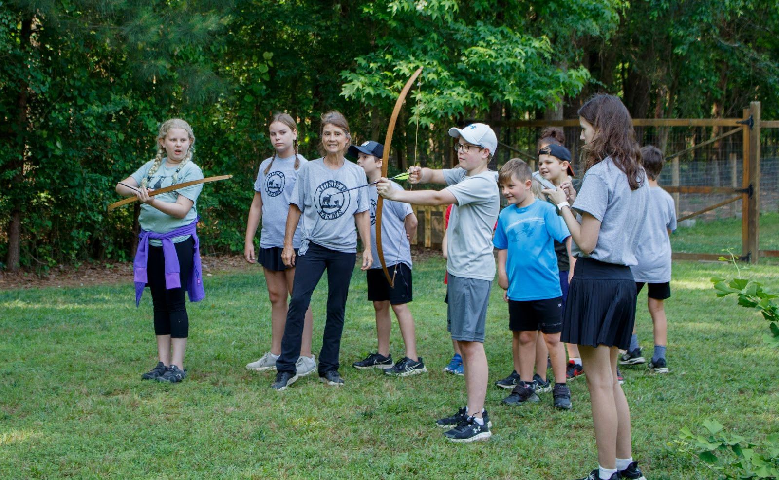 A group of children are standing in a field holding bows and arrows.