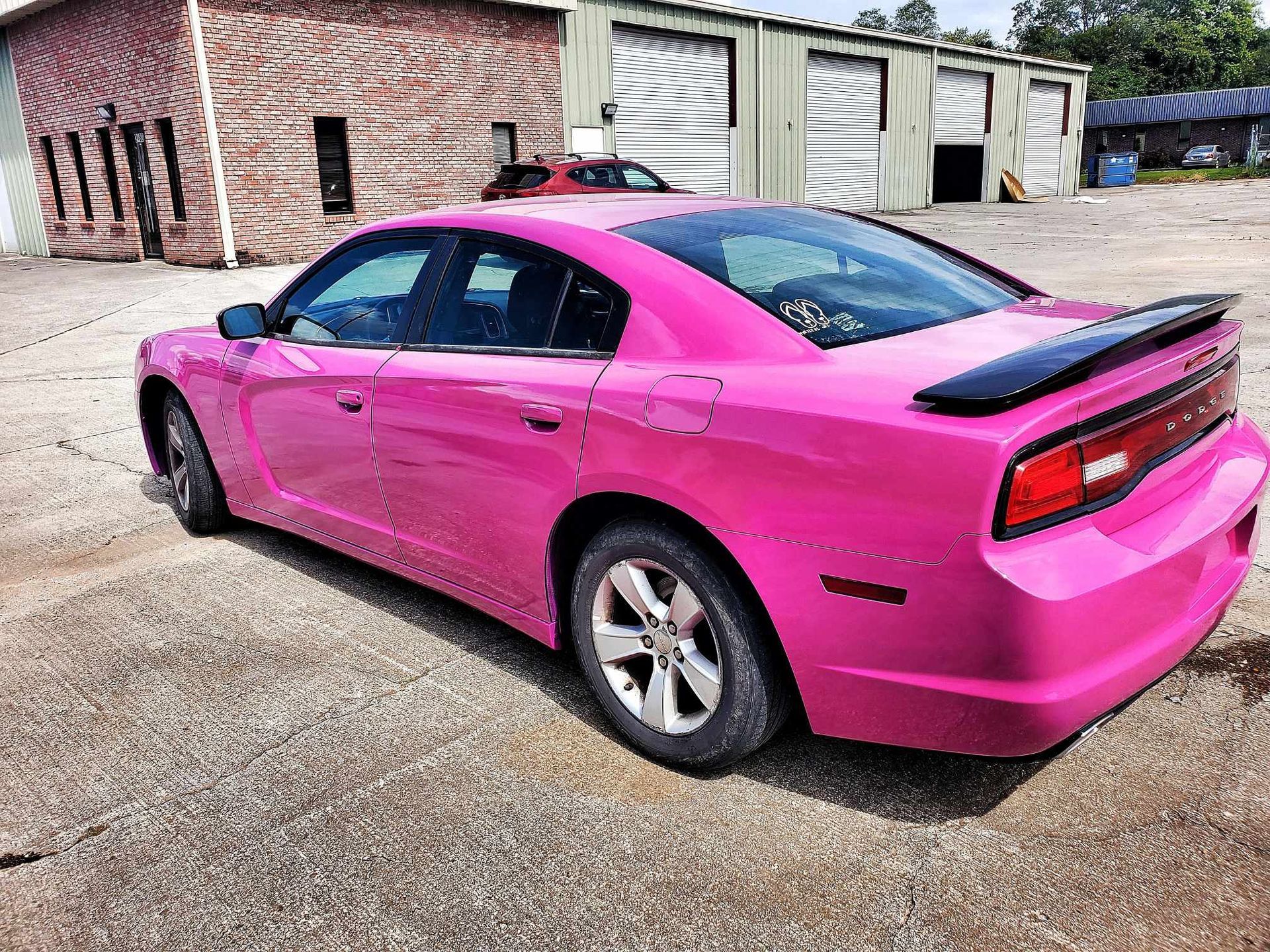 A pink dodge charger is parked in a parking lot in front of a building.