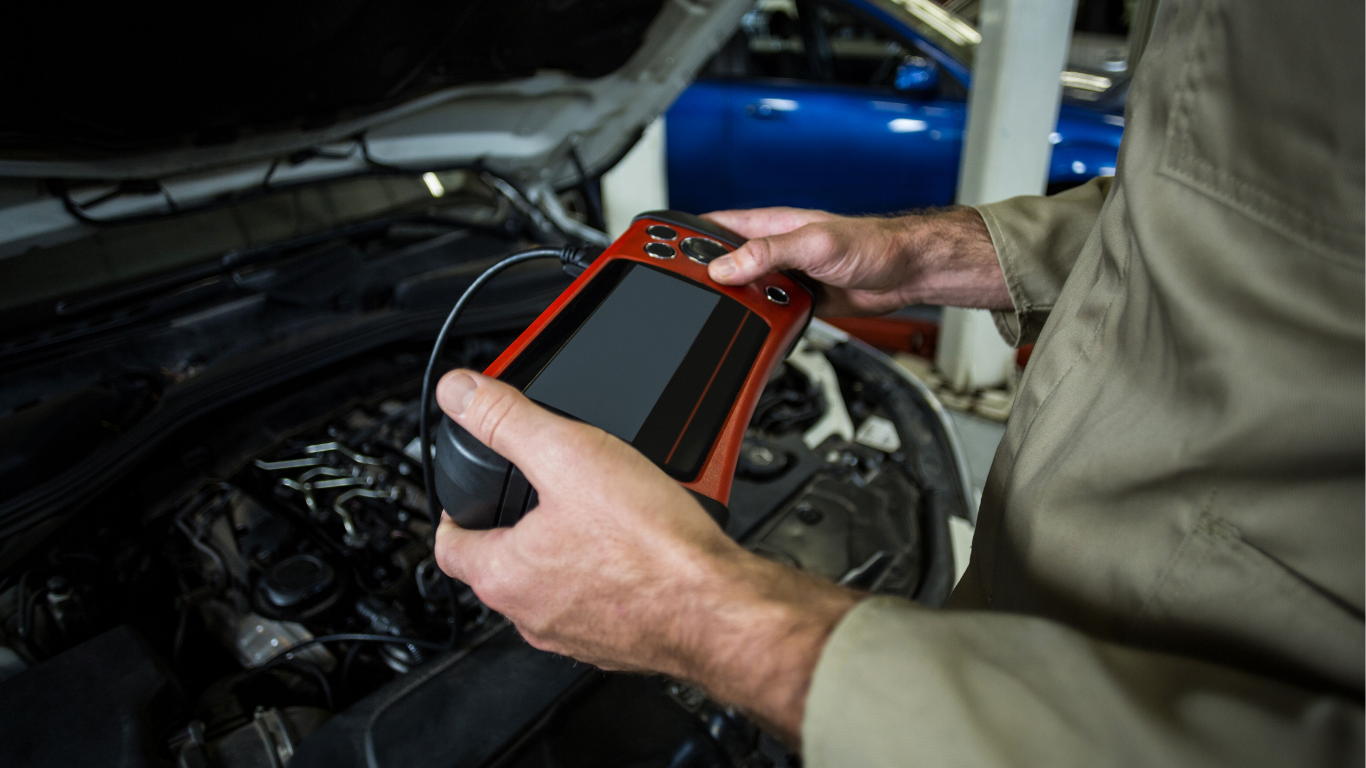 Mechanic uses diagnostic tool on a car engine in a garage.