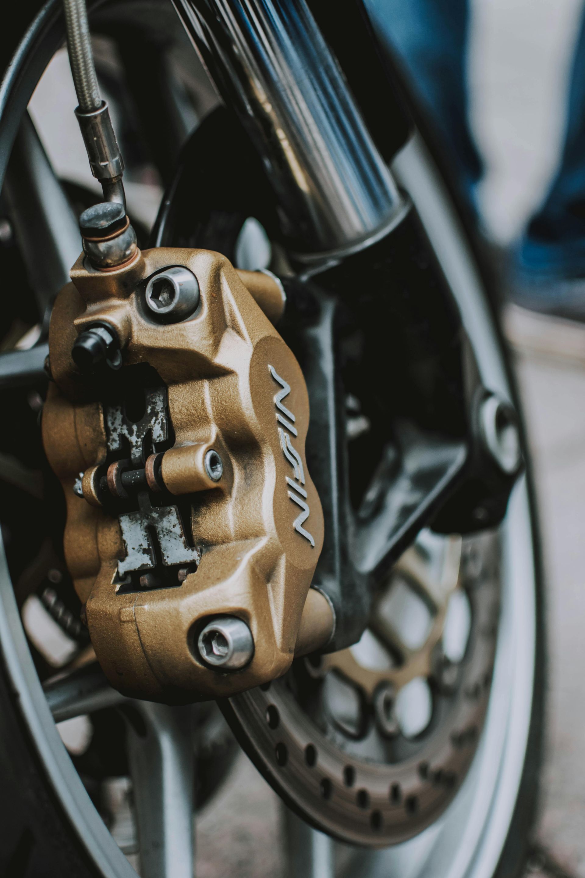 Gold-colored Nissin brake caliper on a motorcycle's front wheel, with brake disc and suspension components.
