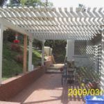 A white pergola is sitting on top of a patio next to a house.