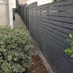 A black wooden fence along a sidewalk next to a house.