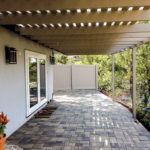A patio with a pergola over it and a fence in the background.