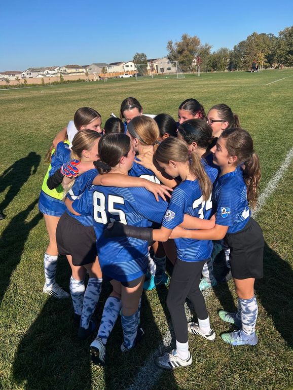 A person wearing a hat and orange shirt, holding a baseball bat on their shoulder on a baseball field.
