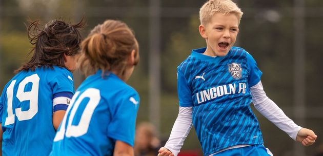 Baseball glove with ball on green grass, with blurred baseballs in the background.