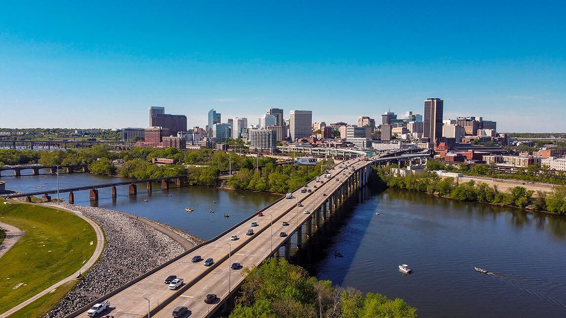 City skyline with a bridge over a river, cars driving on the bridge under a blue sky.