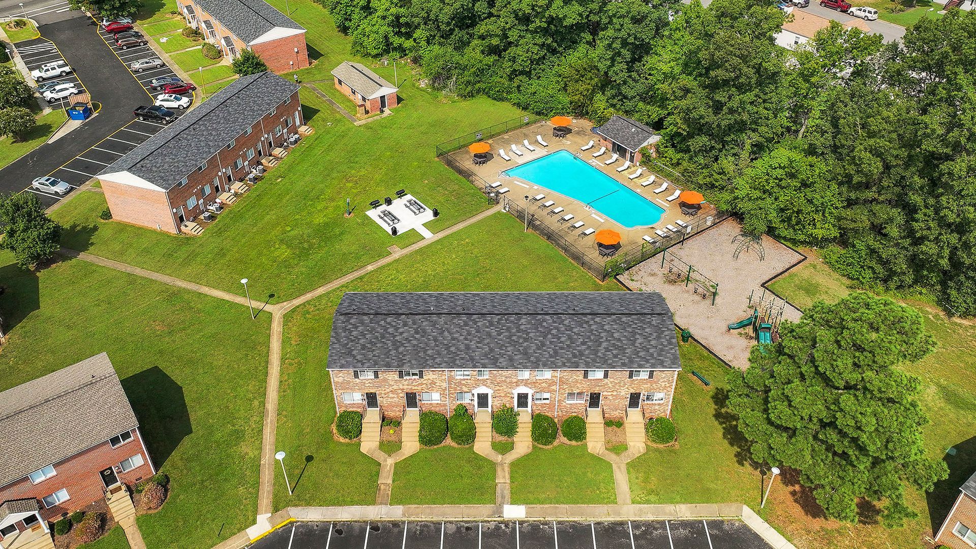 Aerial view of apartment complex with a pool, parking, and green space.