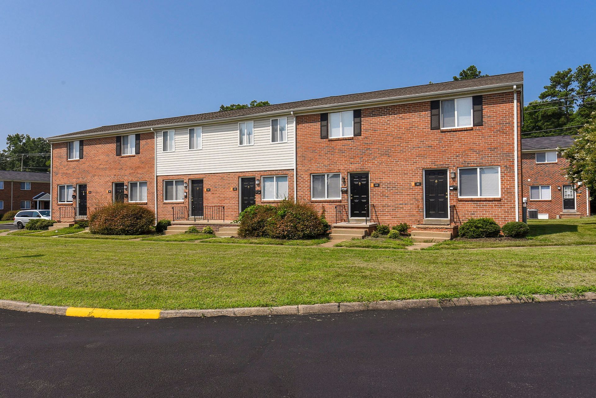 Row of brick townhouses with black doors and white-trimmed windows; blue sky.