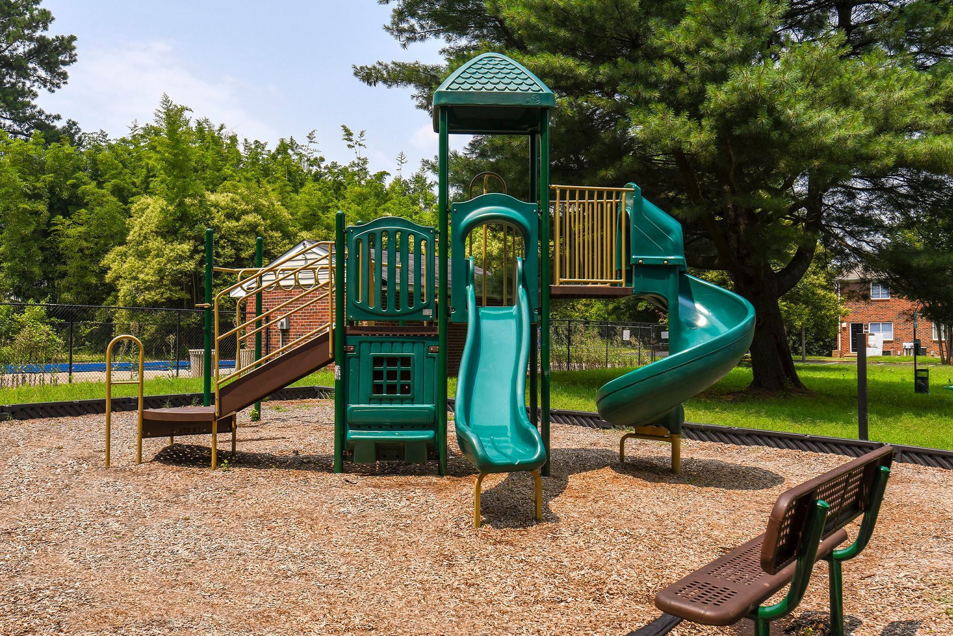 Playground with a green and blue slide, brown stairs, and a bench on wood chips.