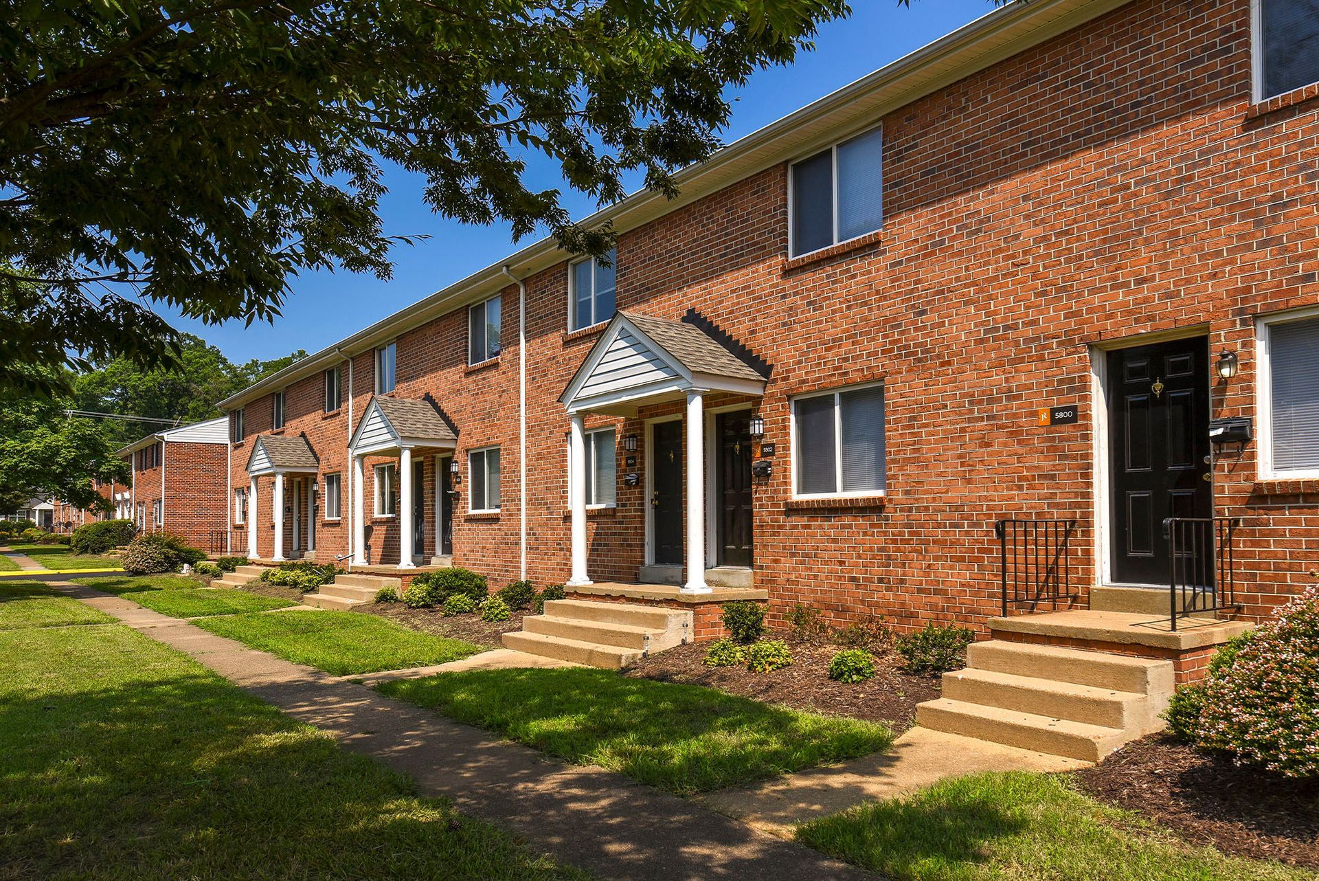 Brick row houses with green lawns and a sidewalk on a sunny day.
