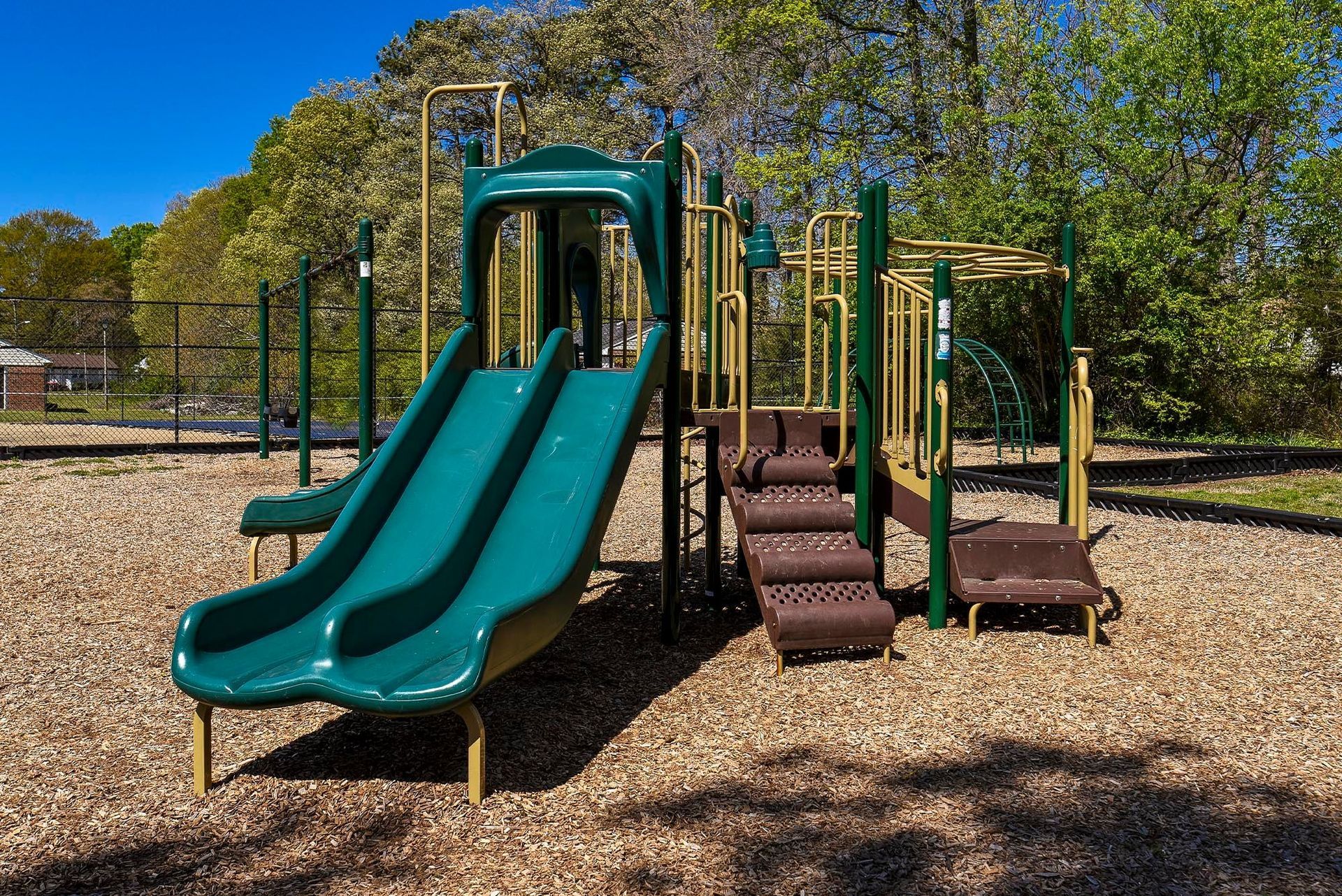 Playground structure with green slide, stairs, and monkey bars, on a bed of wood chips.