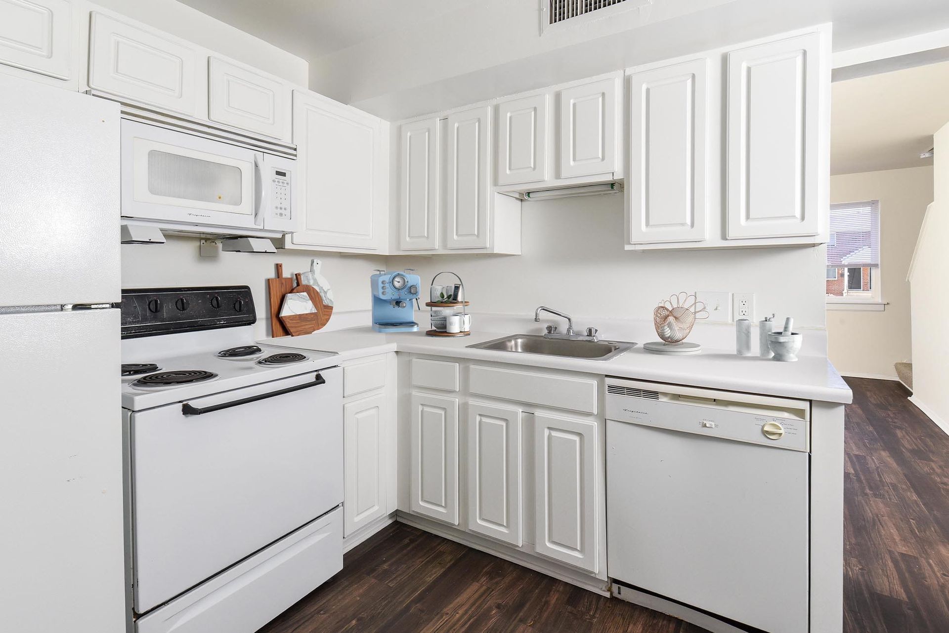 White kitchen with appliances, cabinets, and dark wood-look floor.