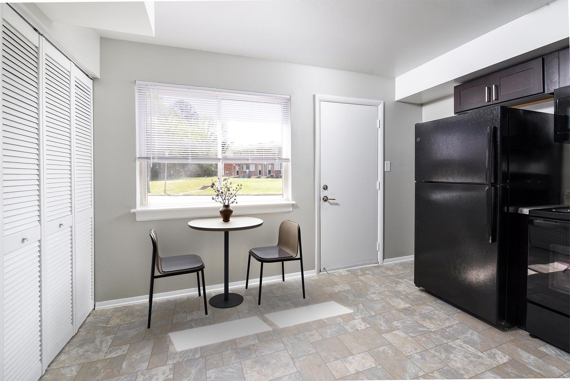 Kitchen with table, chairs, black appliances, window, and closed white doors. Gray walls and flooring.