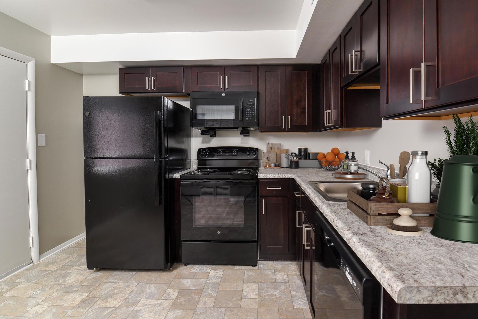 Black appliances in a kitchen with dark cabinets, light countertops, and beige tiled floor.