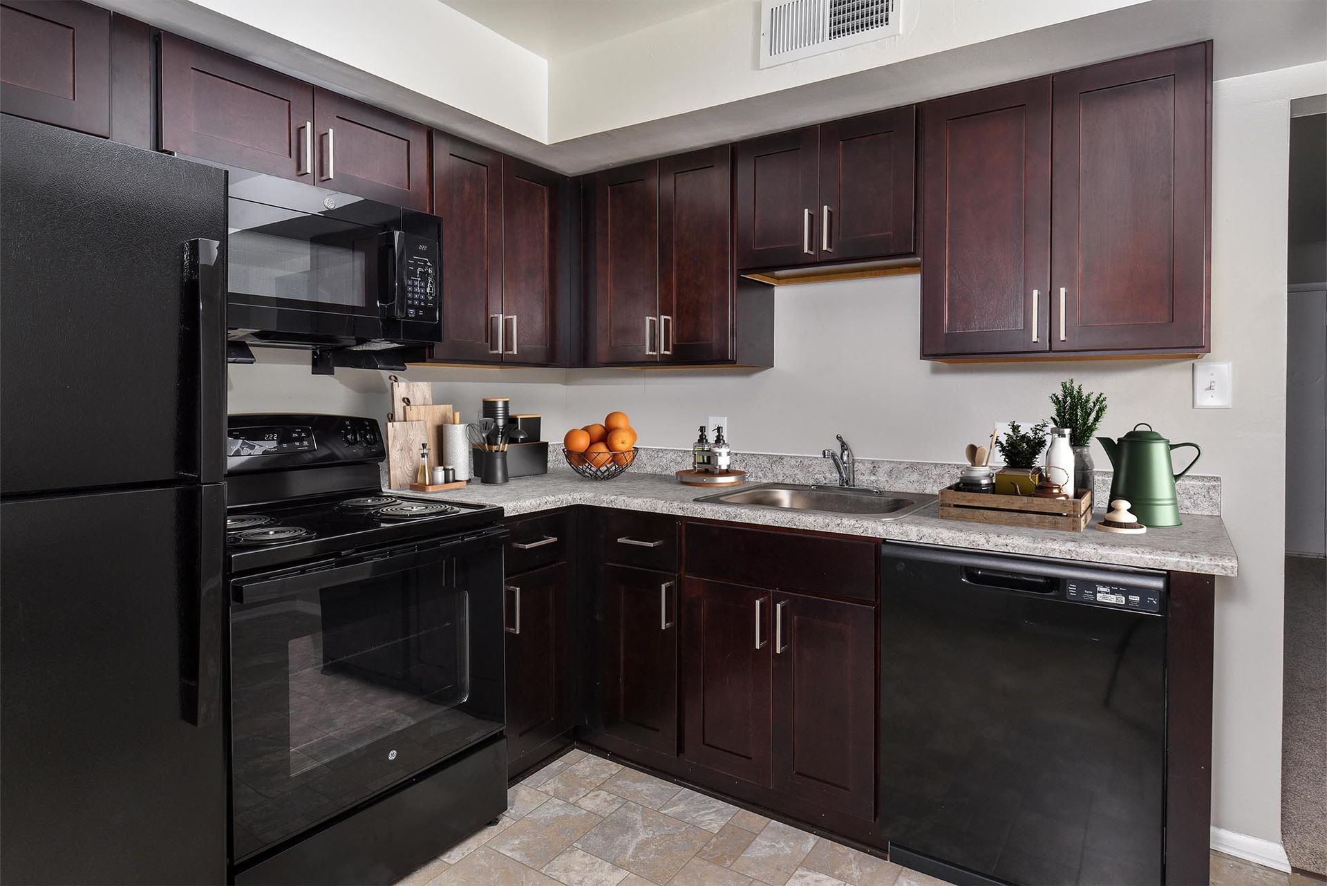 Kitchen with dark brown cabinets, black appliances, and a gray countertop.