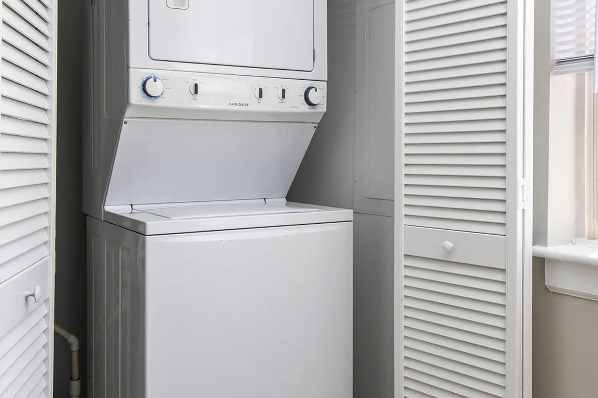 Stacked white washer and dryer units inside a closet with louvered doors.