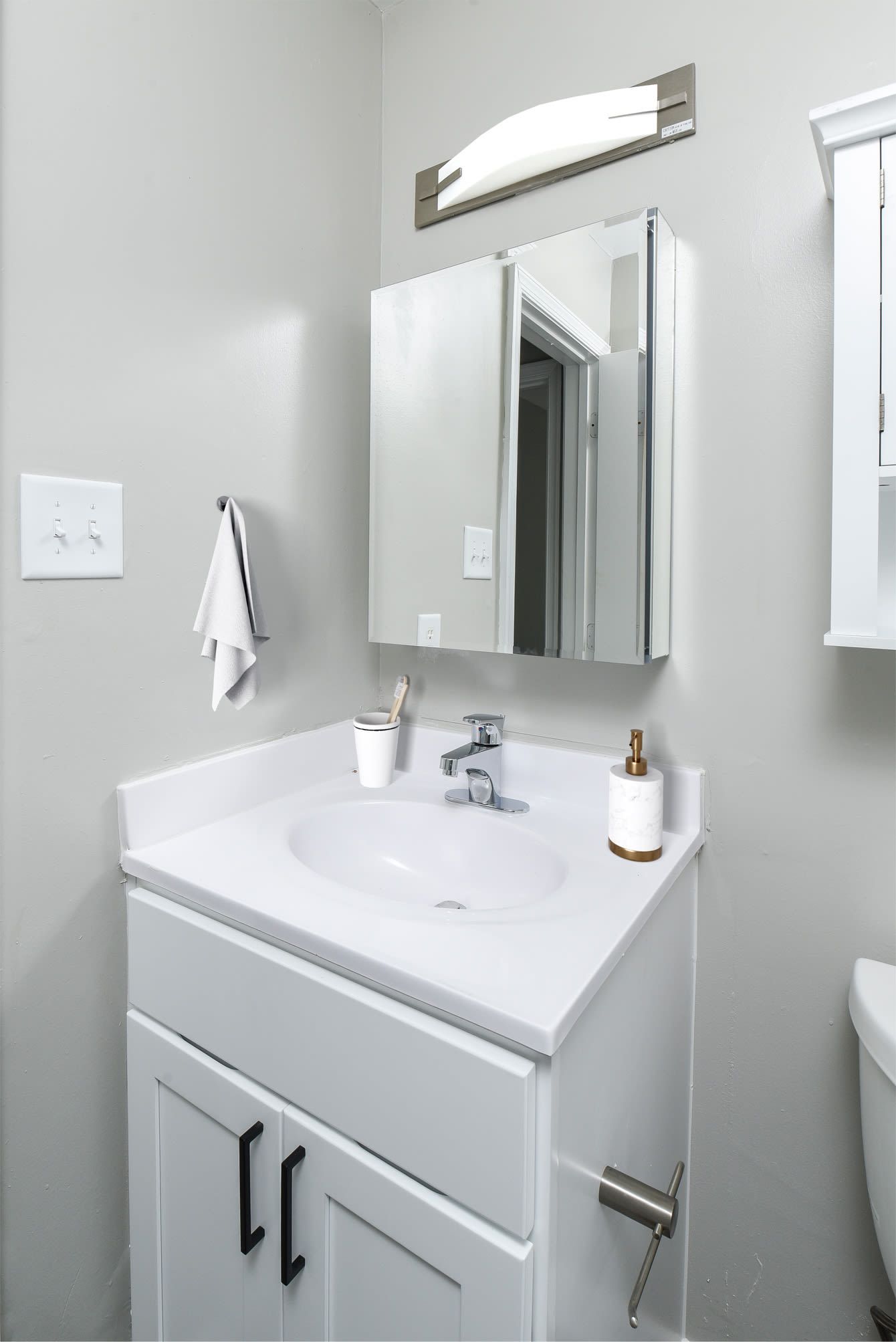 Small white bathroom with sink, mirror, and toilet. Gray walls.