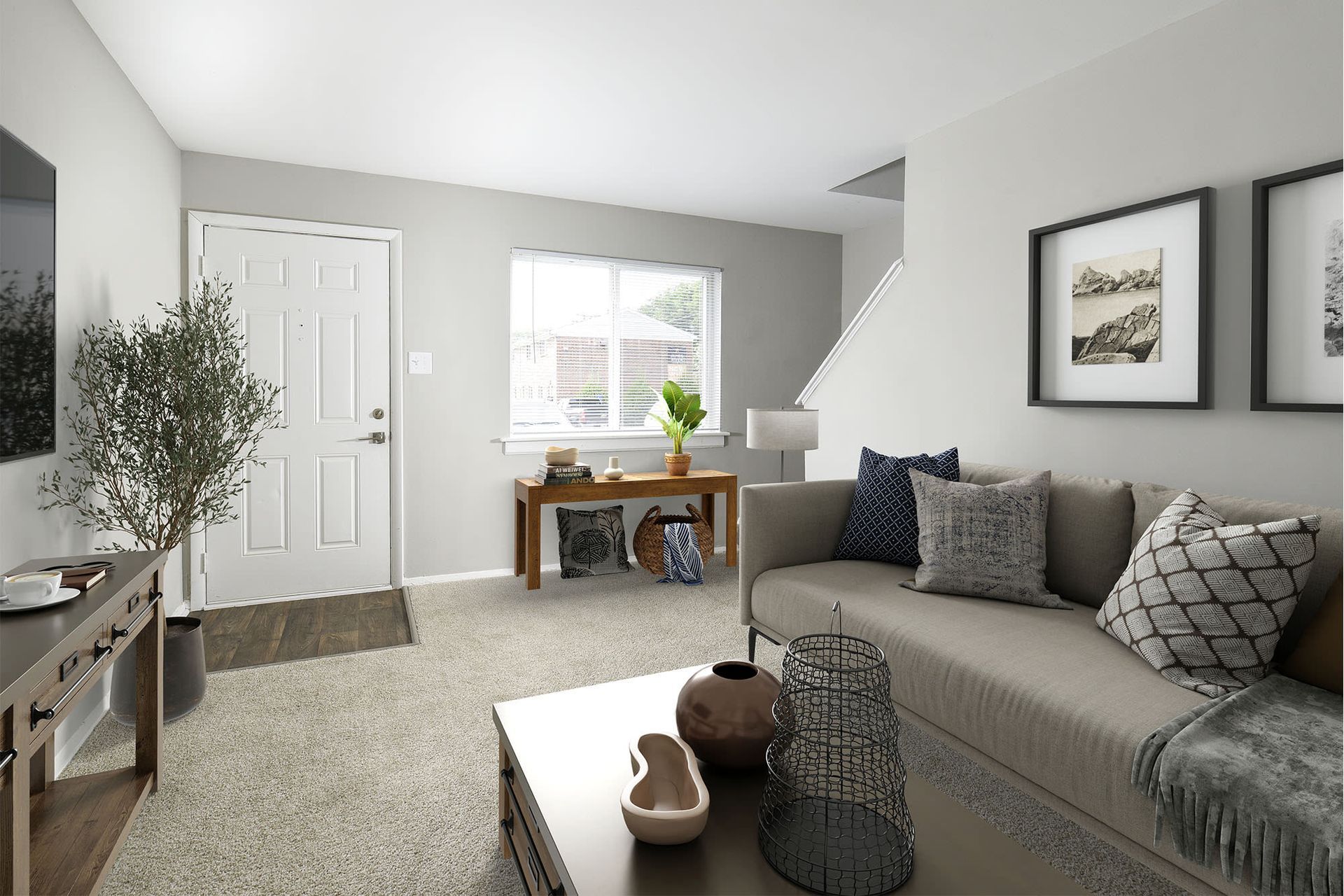 Living room with couch, coffee table, and console table. Door, window, and stairs visible.