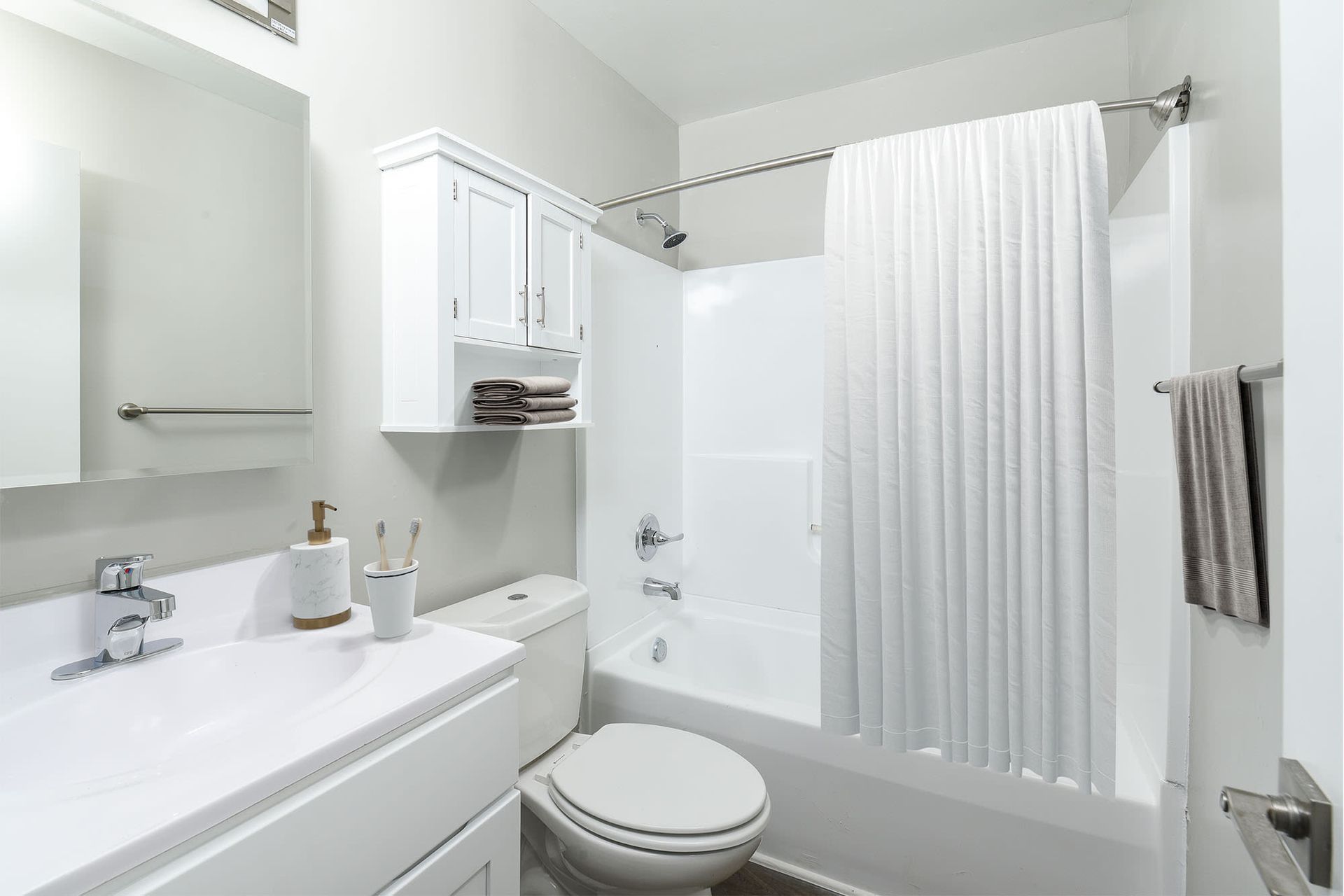 White bathroom with a sink, toilet, tub/shower, cabinet, and towel rack.