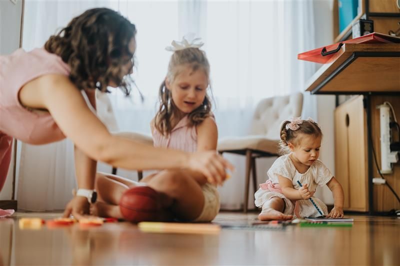 A woman and two little girls are sitting on the floor playing with toys. Text overlaid reads children and young people services. Empowering youth and families through compassionate, specialised case management, our Children and Young People Team provides expert support for a wide range of clinical needs, ensuring every child reaches their full potential.