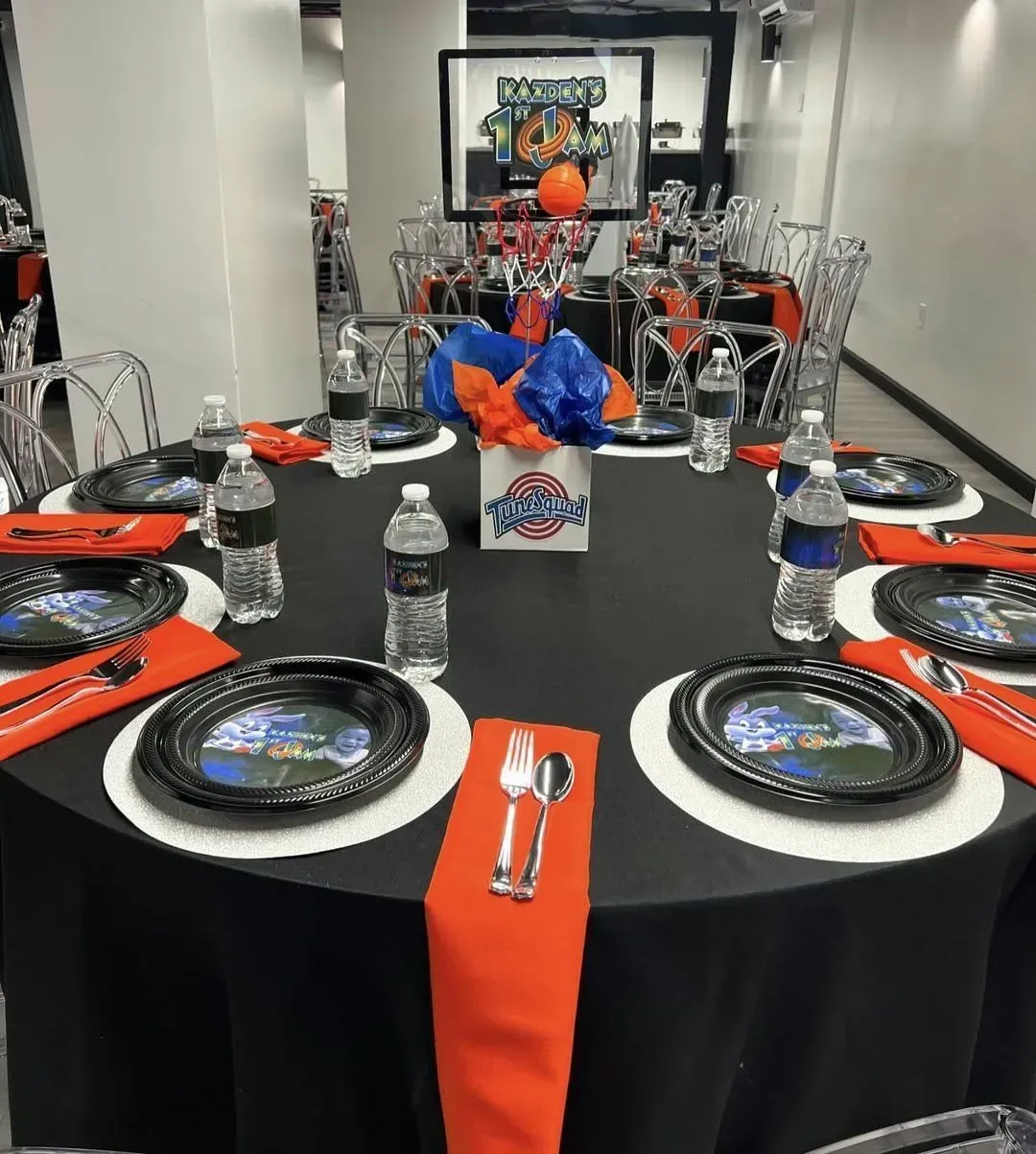 Decorated banquet table with black tablecloth, orange accents, plates, silverware, and water bottles
