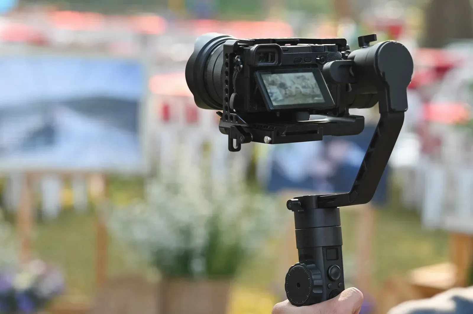 Handheld camera on a gimbal filming an outdoor event with blurred banners