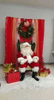 Santa claus is sitting in a chair in front of a christmas wreath.