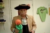 A man in a pirate hat is holding a green balloon with a pumpkin on it.