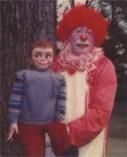 A clown is holding a doll and posing for a picture.