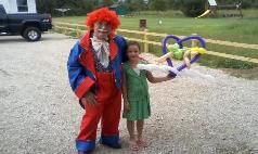A clown is standing next to a little girl holding balloons in the shape of a heart.