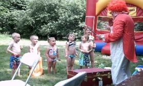 A clown is standing in front of a group of children in front of a bouncy house.
