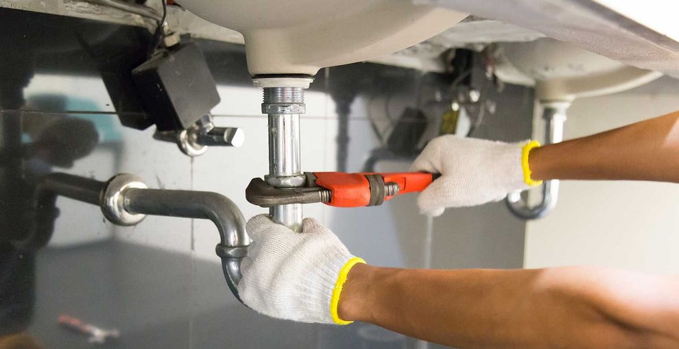 Plumber fixing white sink pipe with adjustable wrench.