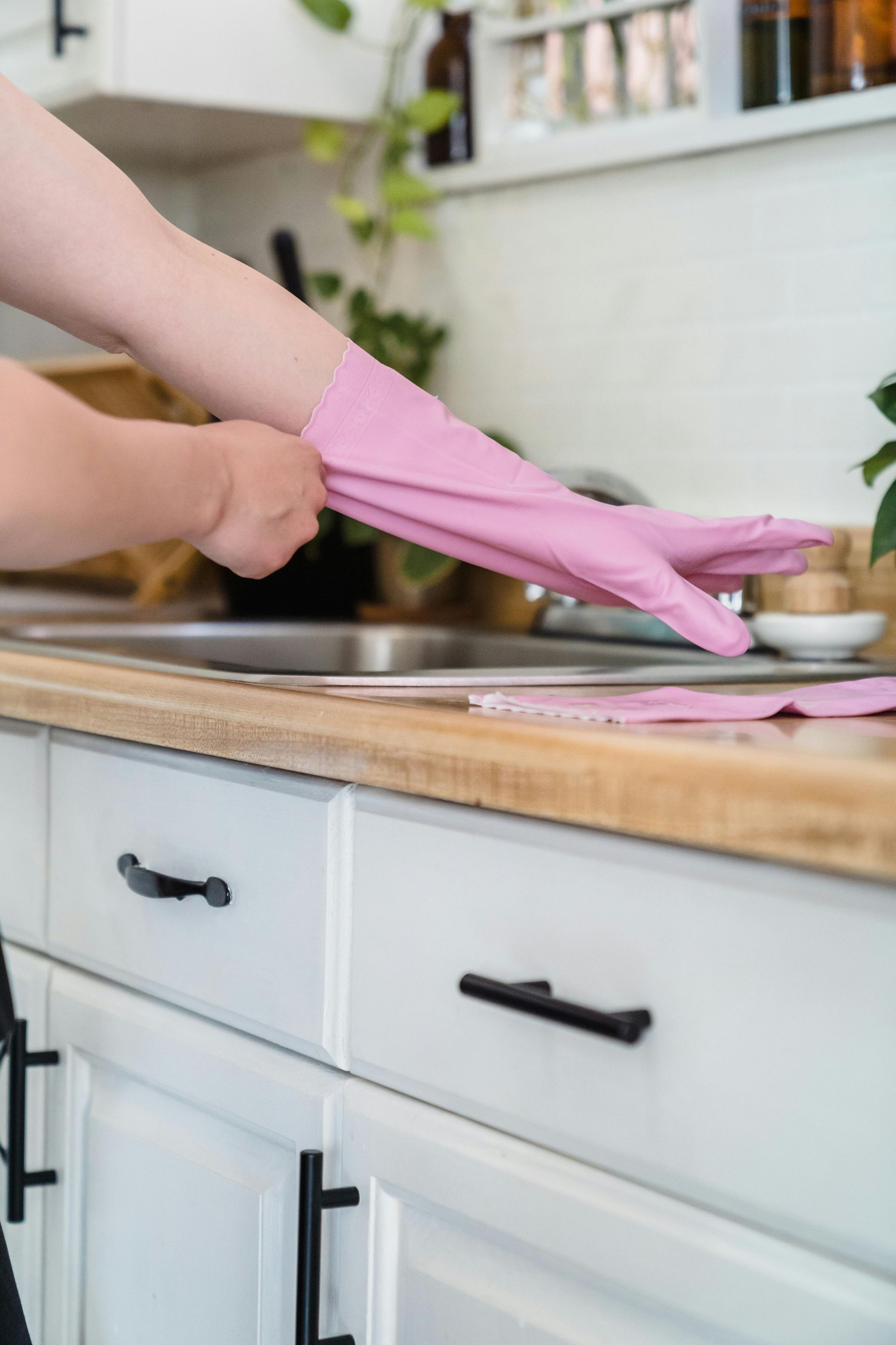 Person putting on pink rubber cleaning gloves in a white kitchen.