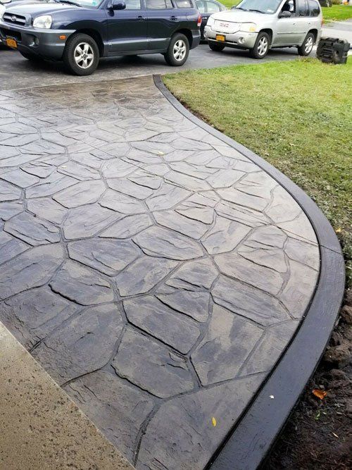 Stamped concrete driveway with a dark stone pattern, curved edge, and vehicles parked nearby.