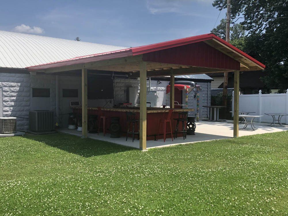 A covered patio with a red roof and a bar in the backyard of a house.