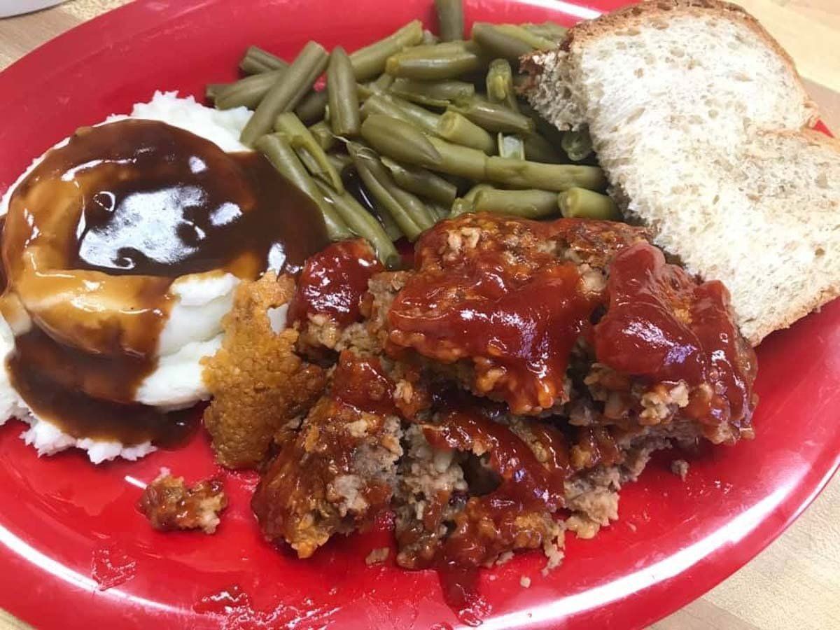 A red plate topped with meatloaf mashed potatoes green beans and bread