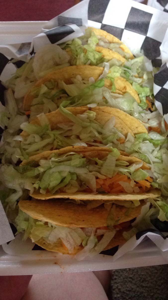 A person is holding a styrofoam container filled with tacos and lettuce.