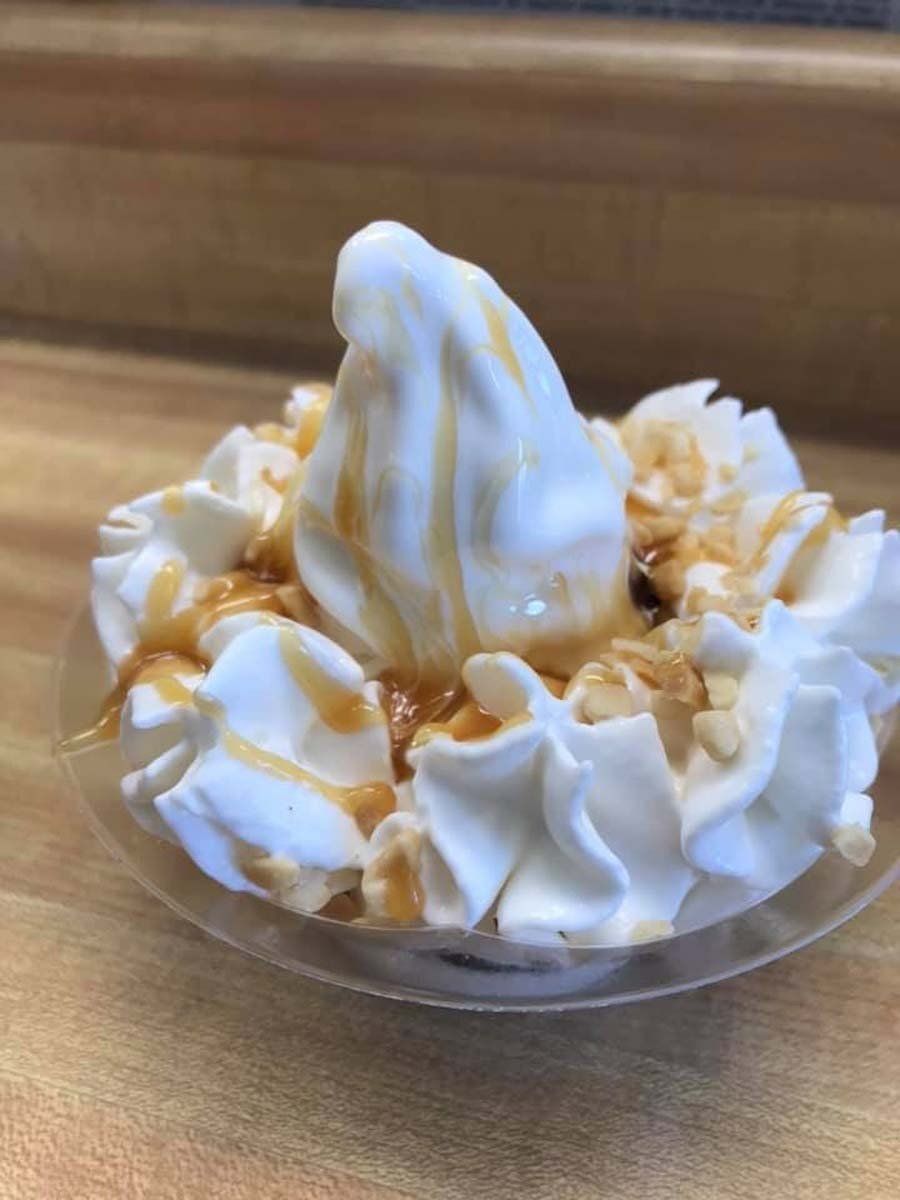 A close up of a bowl of ice cream with whipped cream and caramel sauce.