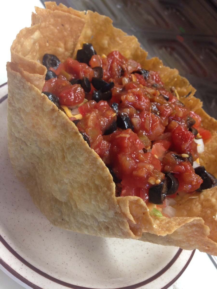 A close up of a taco with tomatoes and olives on a plate