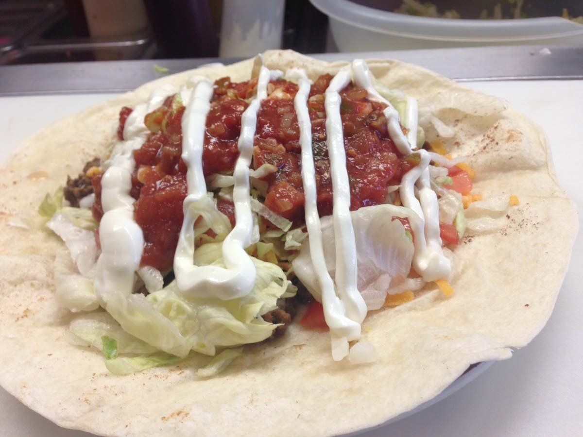 A burrito with lettuce , tomatoes , cheese and sour cream on a plate.