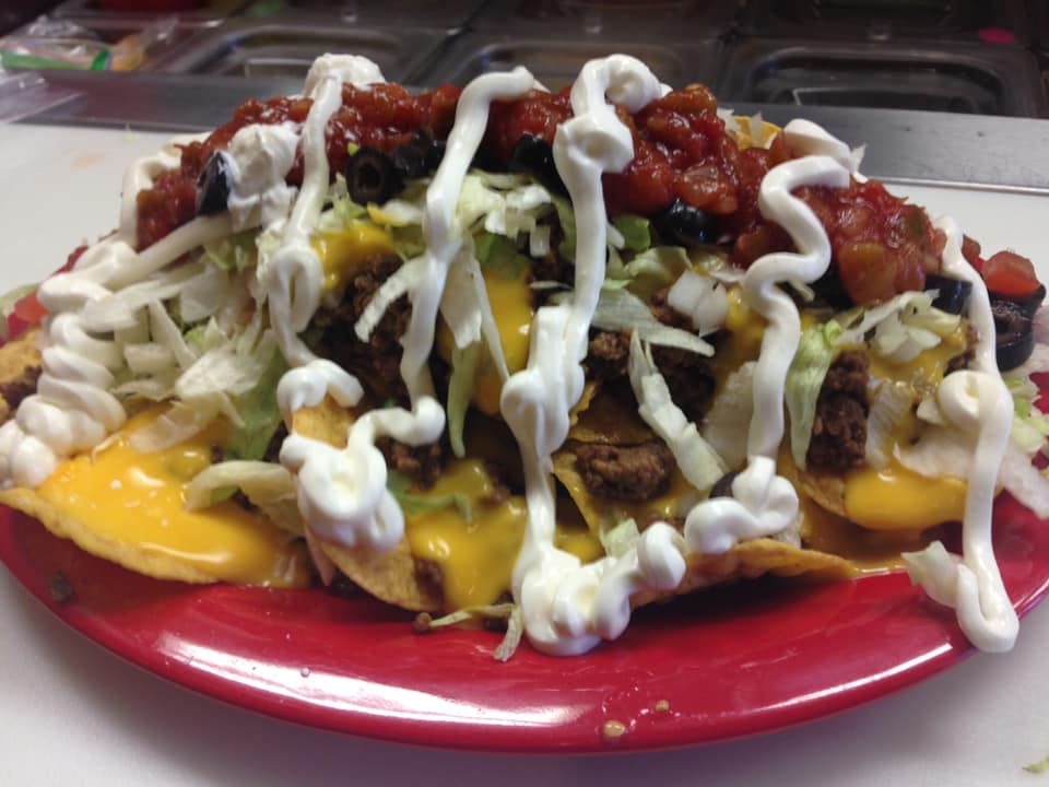 A close up of a plate of nachos with sour cream on top