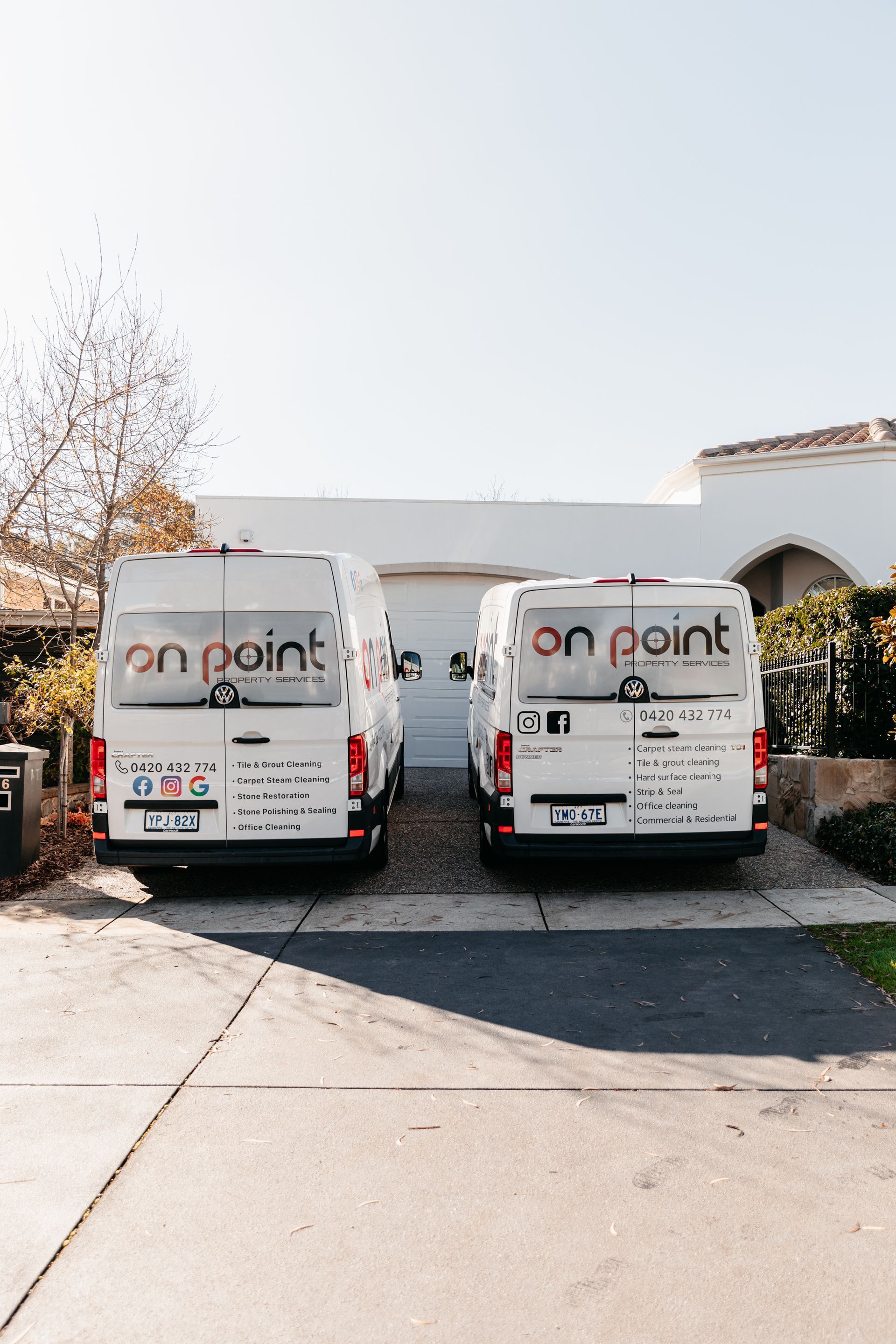 Two white vans are parked in a driveway in front of a house.