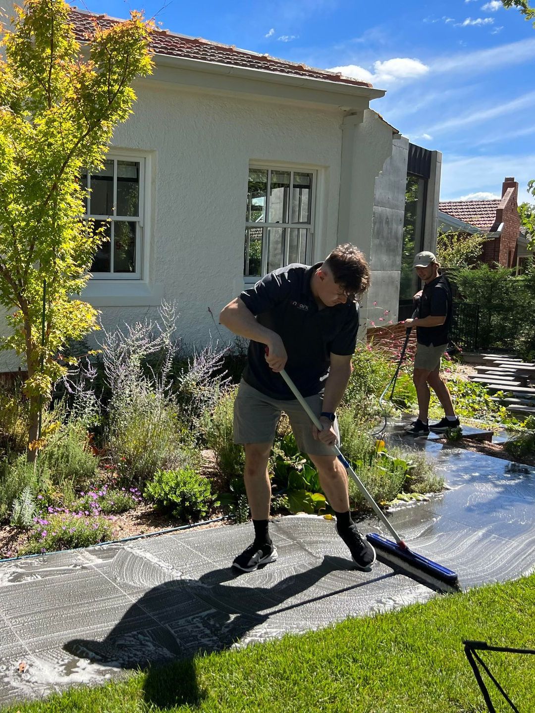 A man is sweeping the sidewalk in front of a house.