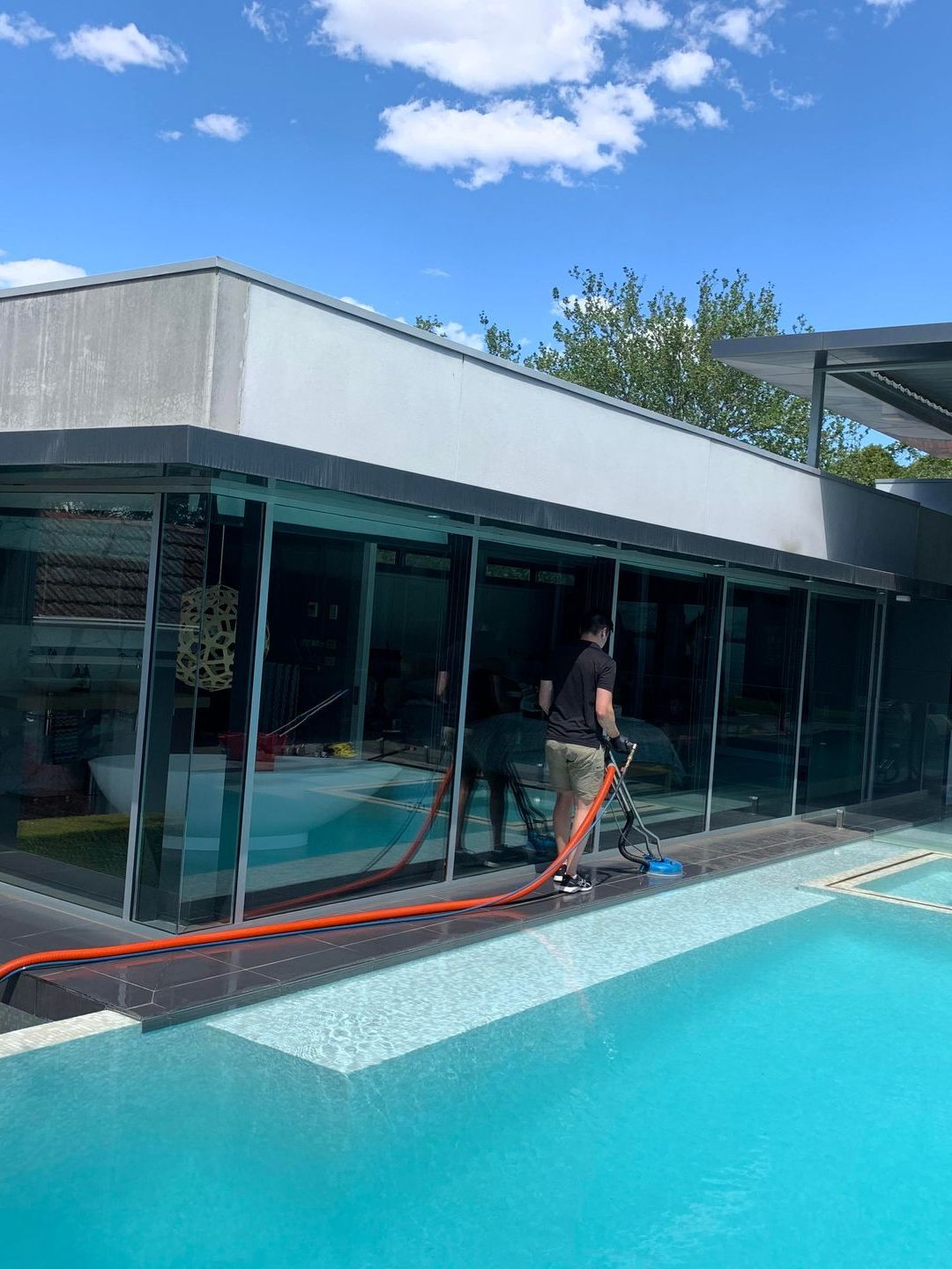 A man is cleaning the windows of a building next to a swimming pool.