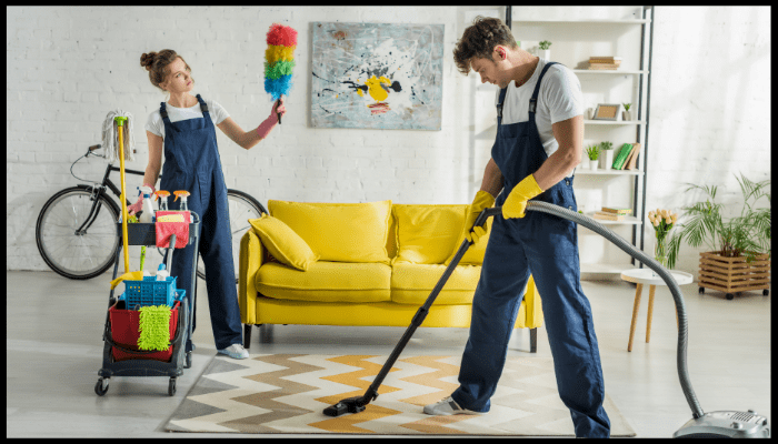 A man and a woman are cleaning a living room with a vacuum cleaner.